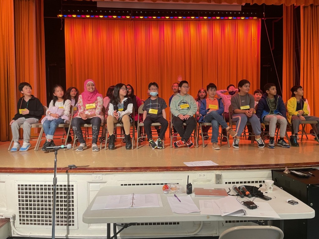 Two rows of students sit on the stage for the spelling bee