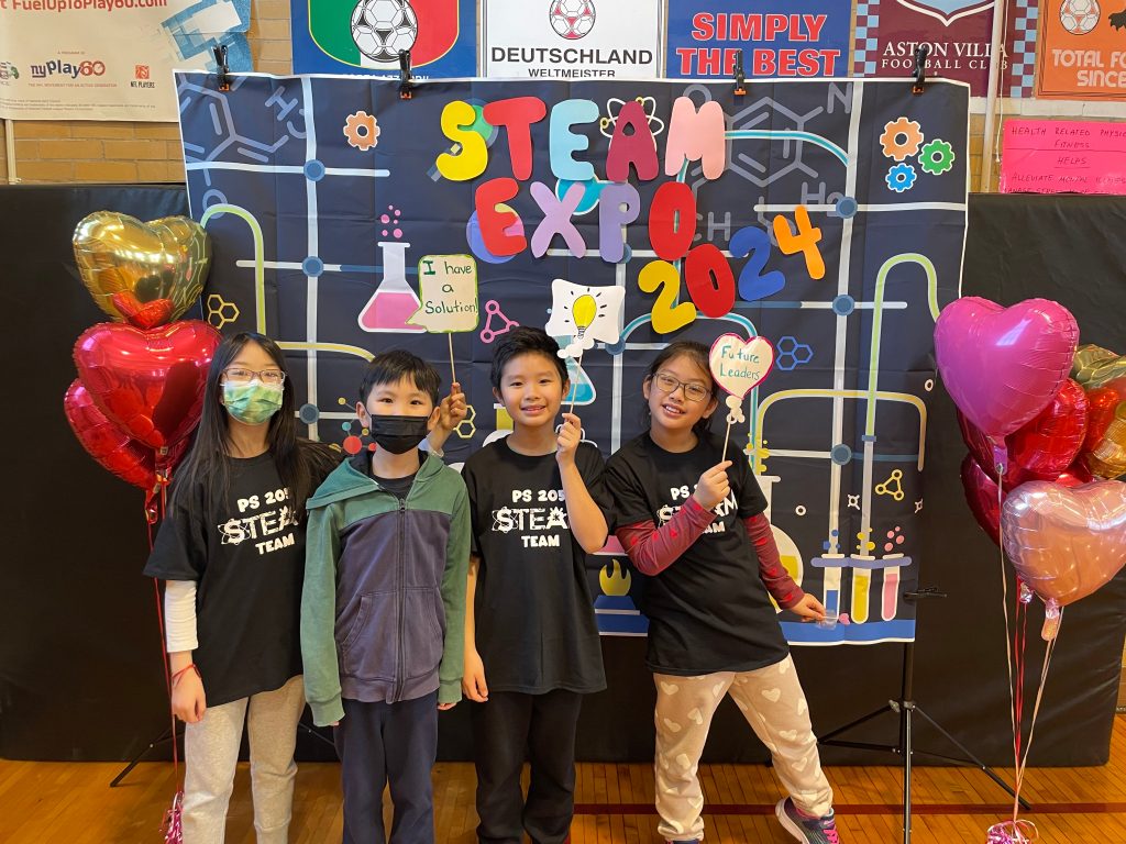 Students in black STEAM team shirts posing in front of the a Steam Expo display